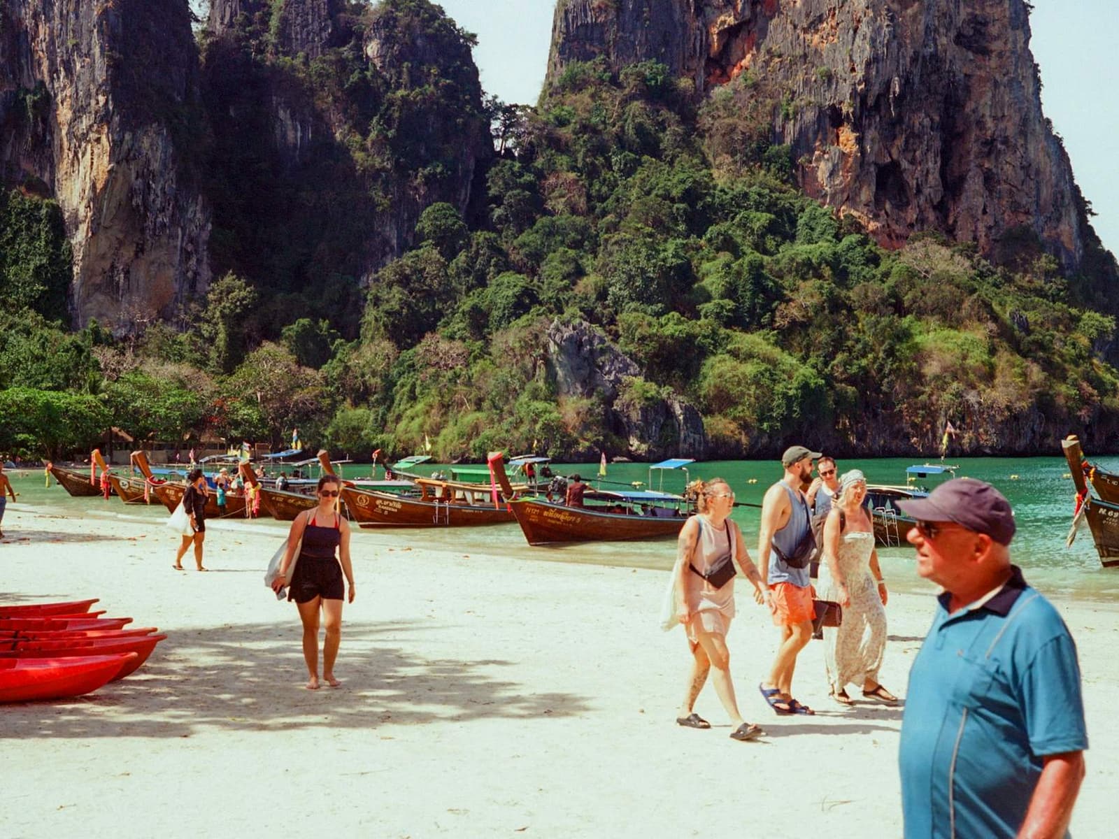 Travelers walking a beach lined with longtail boats at Ao Nang